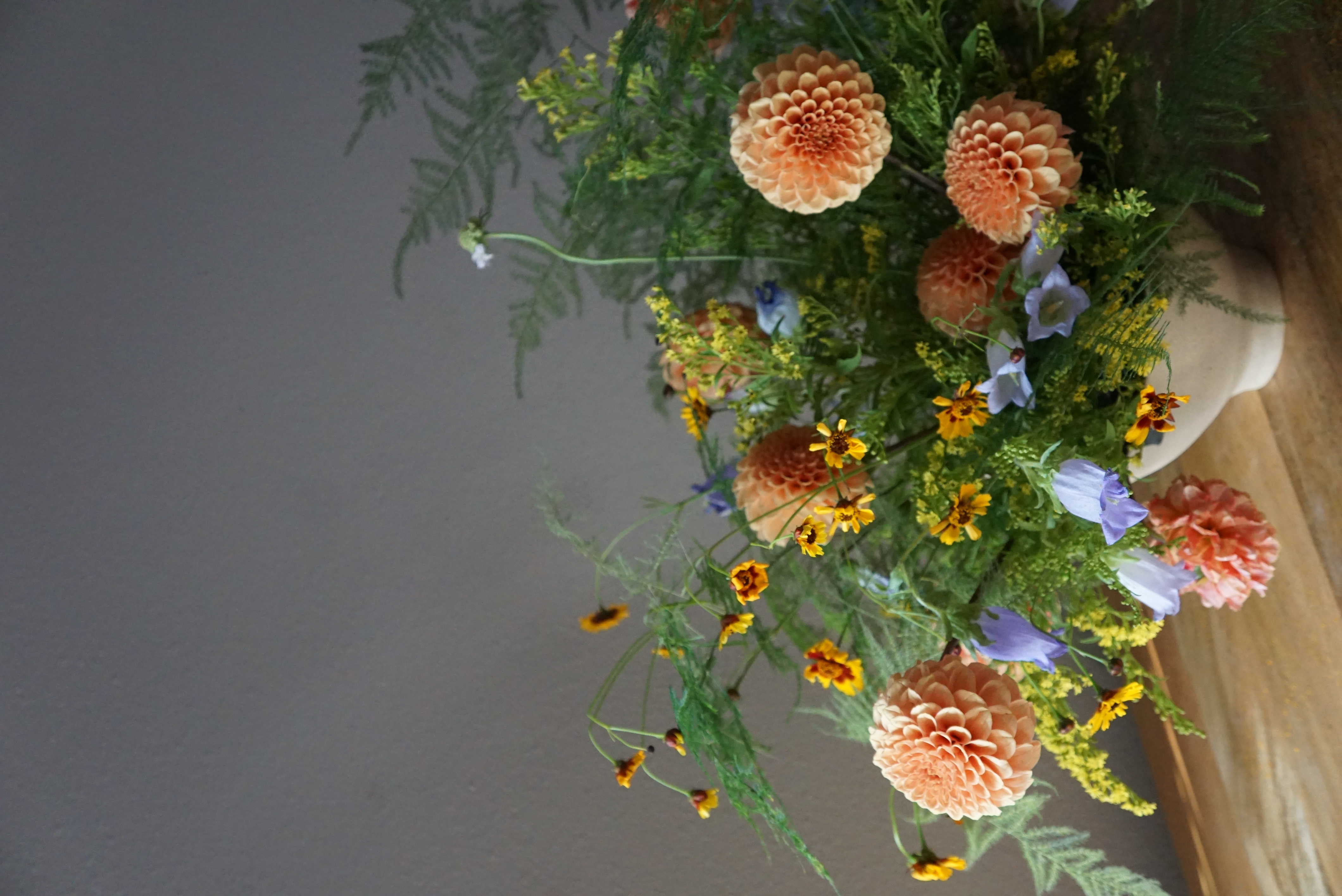 A classic flower arrangement giving meadowy vibes featuring flowy ferns, yellow solidago, peachy dahlias, purple campanula bellflowers, and orange-red coreopsis.