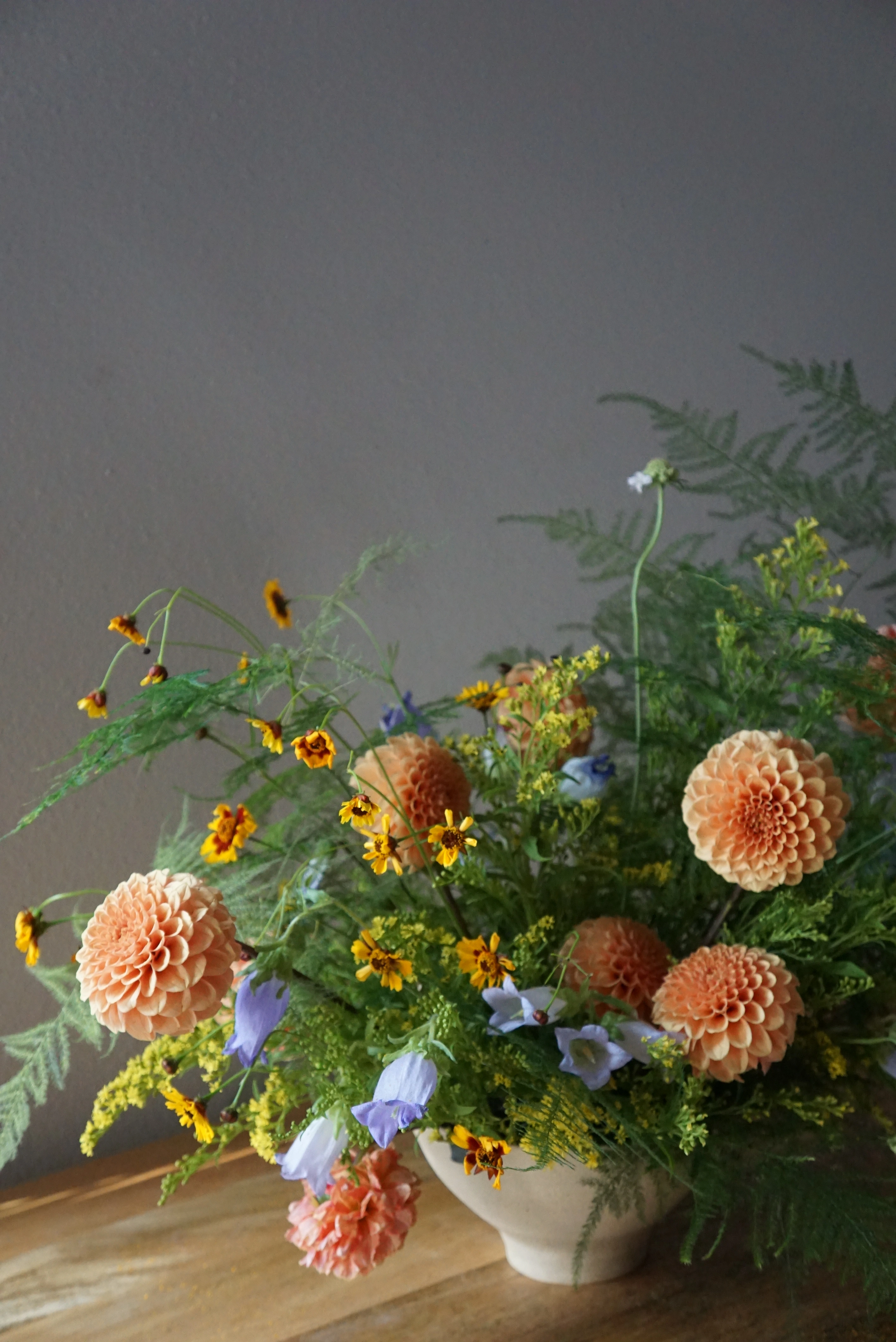 A custom flower arrangement giving meadowy vibes featuring flowy ferns, yellow solidago, peachy dahlias, purple campanula bellflowers, and orange-red coreopsis.